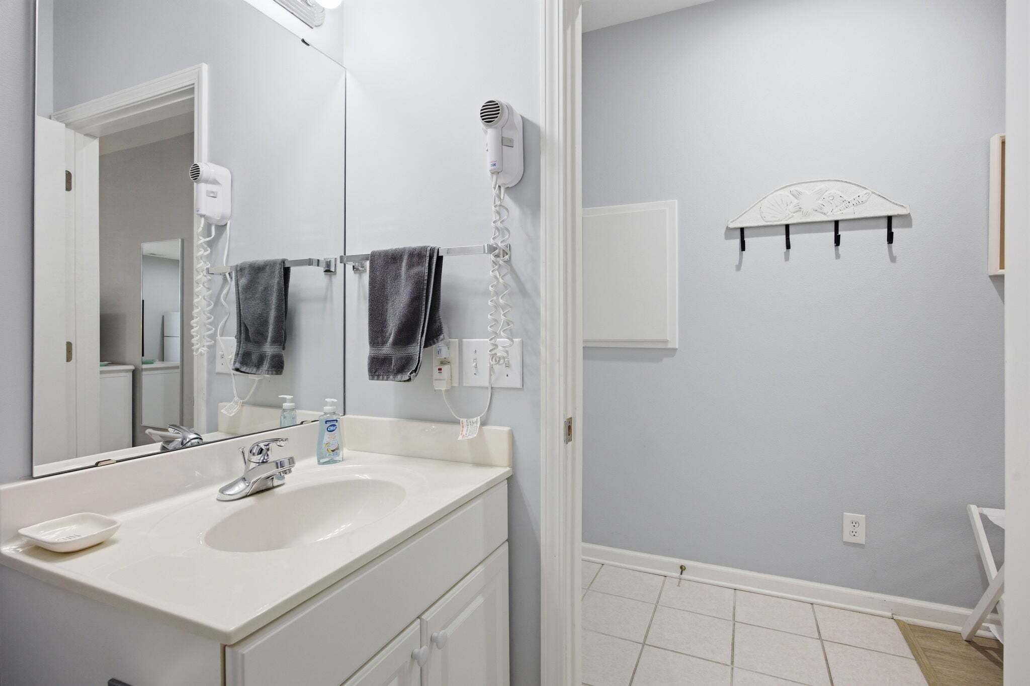 Une salle de bain avec un lavabo blanc, un miroir, un porte-serviettes et un sèche-cheveux.