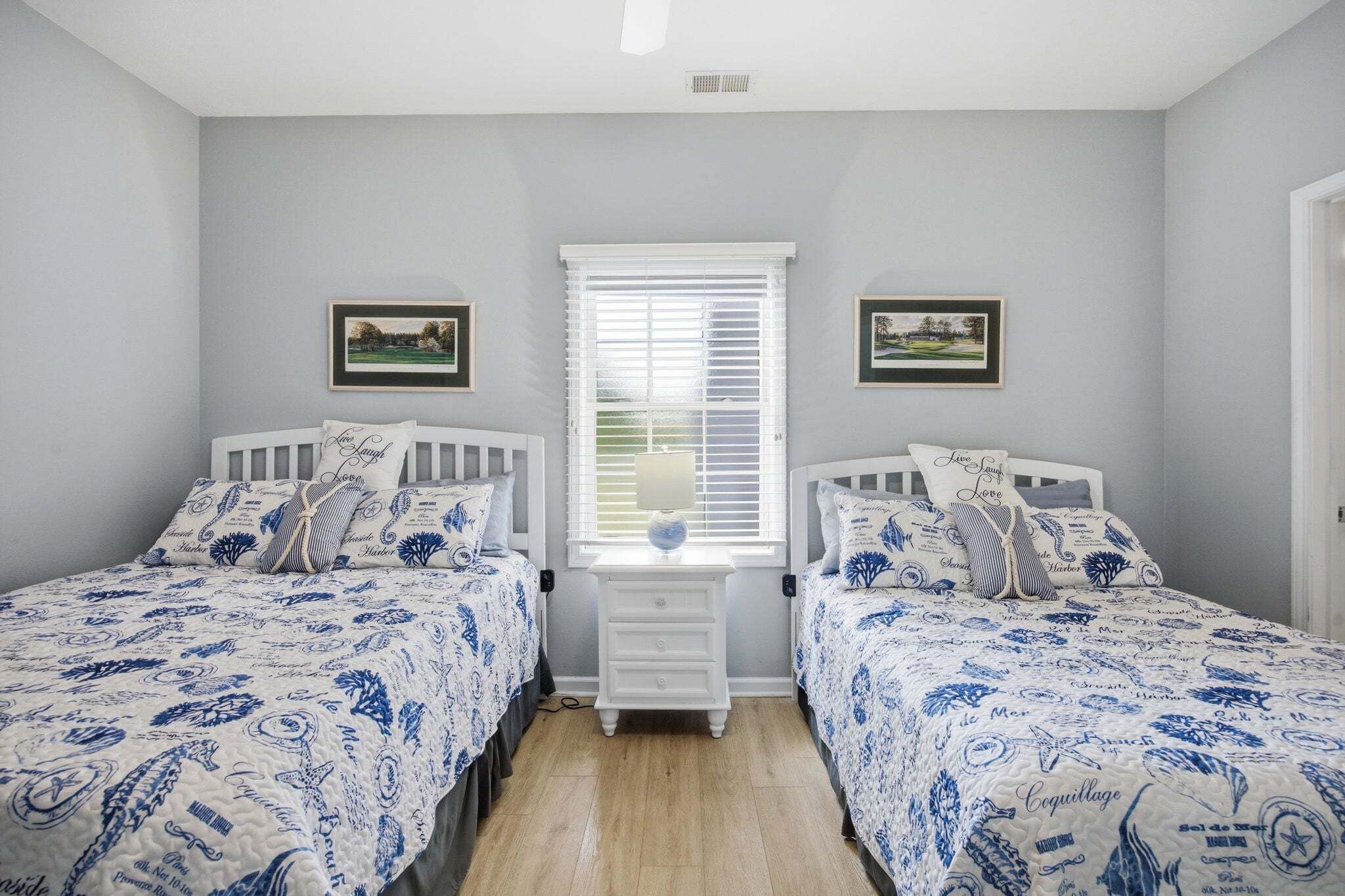 A bedroom with two beds, a nightstand, and a window with blinds.
