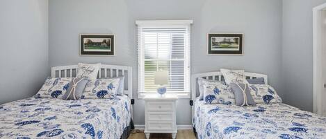 A bedroom with two beds, a nightstand, and a window with blinds.