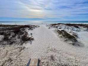 Ein Sandstrand mit einer Holzpromenade, die zum Wasser führt, einem Wegweiser und Dünen.