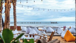 En avslappnad lounge vid stranden med trämöbler, vita kuddar och ljusslingor.