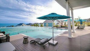 Ett poolområde vid semesteranläggningen med solstolar, parasoller och utsikt över havet.