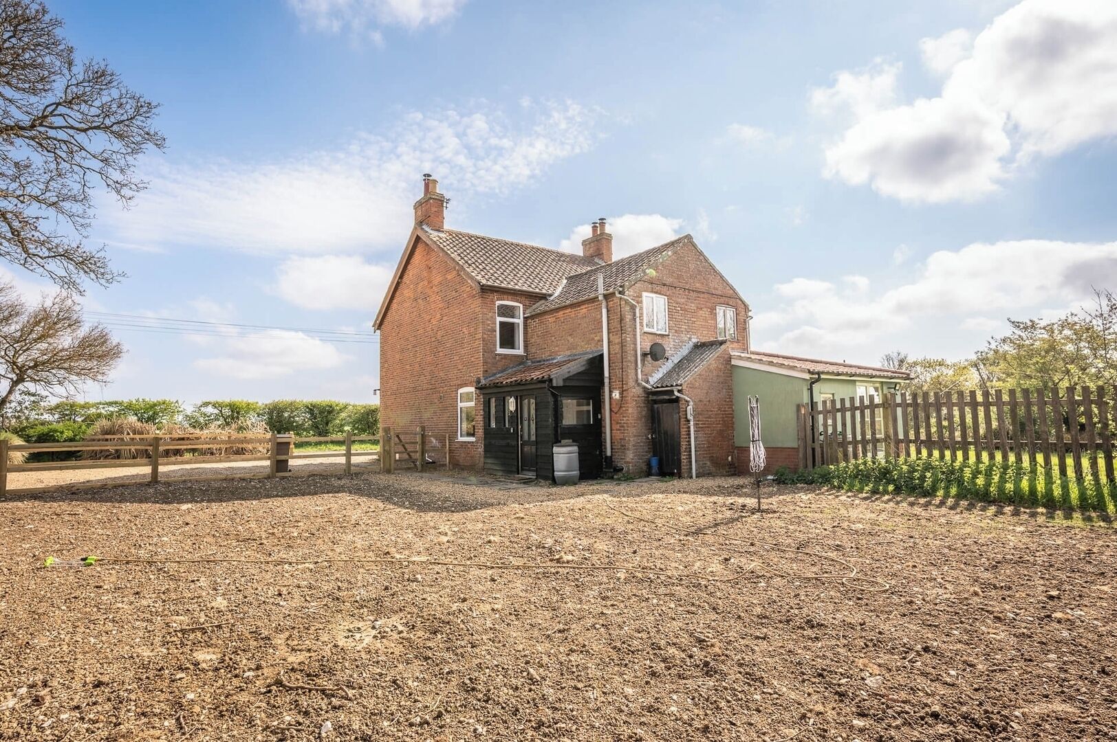 A two-story brick house with a garage, a fenced yard, and a gravel driveway.