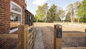 A brick building with a wooden gate, a gravel path, and a sign indicating 'Crossing Cottage.' - 2 Crossing Cottage, Theberton (Leiston)