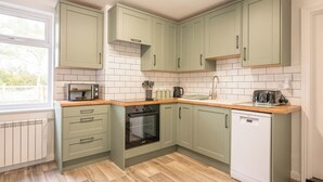A kitchen with light green cabinets, a built-in oven, a dishwasher, and a window providing natural light. - 2 Crossing Cottage, Theberton (Leiston)