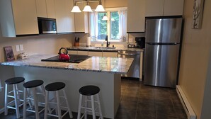 A kitchen with a stainless steel refrigerator, a kettle on the island, and a window with curtains. - Cozy Newly Renovated 3BR Madison Condo Pool + Tennis White Mountains Getaway (Conway)