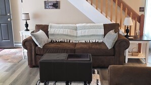 A living room with a brown sofa, a black ottoman, a wooden staircase, and a ceiling fan. - Cozy Newly Renovated 3BR Madison Condo Pool + Tennis White Mountains Getaway (Conway)