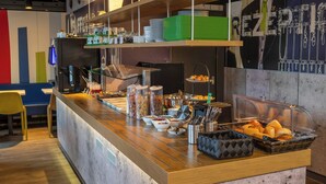 A buffet counter with various food items, utensils, and a seating area with chairs. - B B Hotel Braunschweig West (Braunschweig)