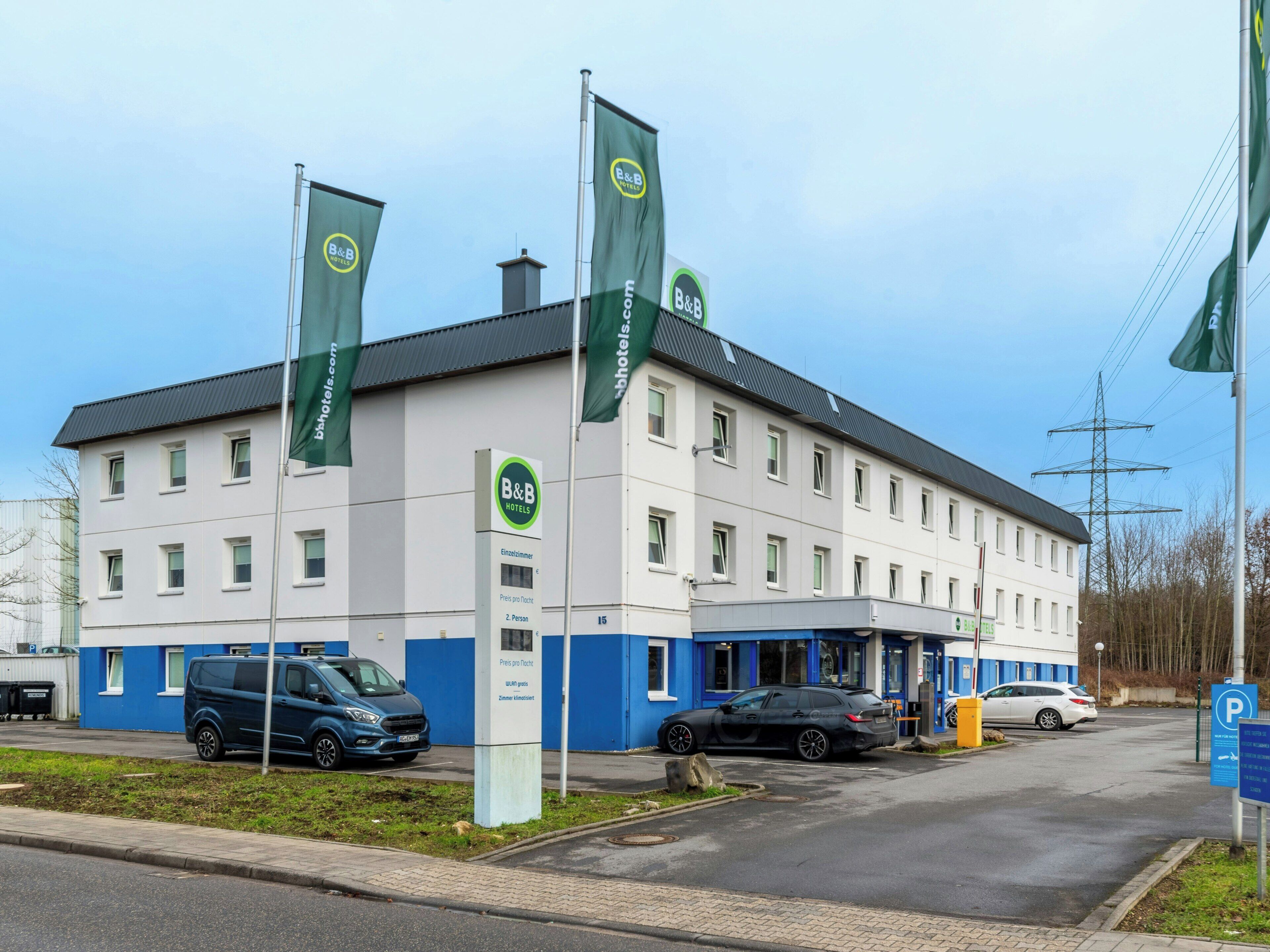 A B&B hotel with a white facade, multiple windows, and a parking area with cars.