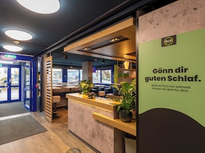 A hotel reception area with a modern design, including a reception desk, seating area, and a view of the street outside. - B B Hotel Braunschweig West (Braunschweig)
