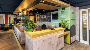 A modern breakfast bar with a wooden counter, seating area, and a green wall with a sign. - B B Hotel Braunschweig West (Braunschweig)