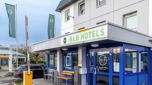 A B&B hotel with a blue facade, a bench outside, and a clear sky. - B B Hotel Braunschweig West (Braunschweig)