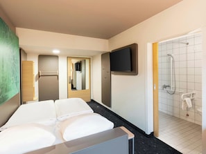 A hotel room with a bed, a TV mounted on the wall, a shower area, and a mirror. - B B Hotel Braunschweig West (Braunschweig)