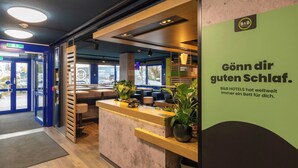 A hotel reception area with a modern design, including a reception desk, seating area, and a view of the street outside. - B B Hotel Braunschweig West (Braunschweig)