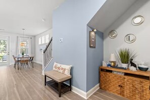 Ein modernes Interieur mit einer Treppe, einem Essbereich mit Tisch und Stühlen, einem Konsolentisch mit Dekoration und einer Wand mit einer Leuchte und Wandspiegeln.