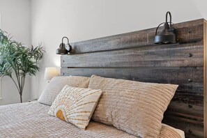 Ein Bett mit Holz-Kopfteil, zwei Wandlampen und einem Blumentopf.