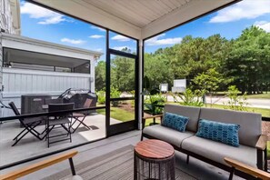 Eine überdachte Terrasse mit einer Couch, einem runden Holztisch und Grillplatz.