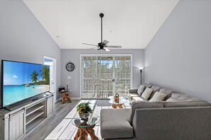 Ein Wohnzimmer mit Fernseher, Sofa, Couchtisch und einem Balkon mit Blick.
