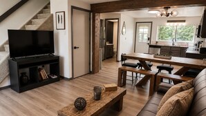 Un soggiorno moderno con televisore, mobili in legno, una scala e una cucina sullo sfondo.
