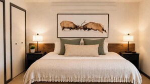 Una camera da letto con un letto grande, due comodini con lampade, un quadro incorniciato al muro e una porta a sinistra.