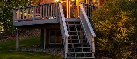 A wooden cabin with a balcony, a staircase leading to the entrance, and string lights.