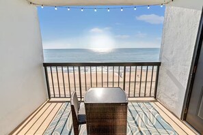 A balcony with a view of the beach, a wicker chair, and a small table. - Oceanfront Condo Balcony N Myrtle Beach (North Myrtle Beach)