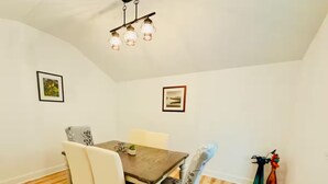 A dining area with a wooden table, white chairs, and a hanging light fixture. - Elton Home (Goldsboro)