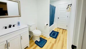 A bathroom with a white sink, toilet, and shower. There are two blue mats on the floor. - Elton Home (Goldsboro)