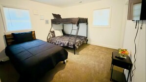 A bedroom with a bed, a bunk bed, a small table with a vase, and a TV mounted on the wall. - Elton Home (Goldsboro)