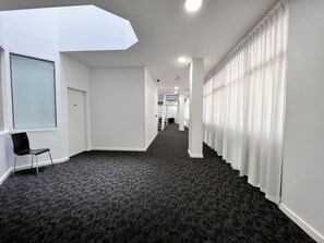 A hallway with a carpeted floor, a black chair, white walls, and a window. - Exhotel city stay 428 (Adelaide)