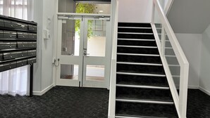 Una hall d'albergo con una scala, scaffali portaoggetti e un cartello di uscita.