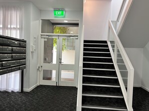 A hotel lobby with a staircase, a set of filing cabinets, and an exit sign. - Exhotel city stay 428 (Adelaide)