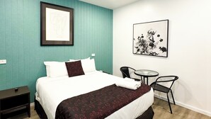 Una camera d'albergo con un letto, una scrivania, una sedia e un quadro appeso al muro.