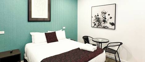 A hotel room with a bed, a desk, a chair, and a wall-mounted picture.