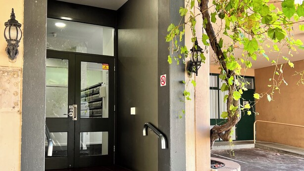 Ingresso di un hotel con una porta scura, gradini che vi conducono e un faretto a parete.
