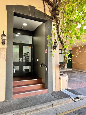 Ingresso di un hotel con una porta scura, gradini che vi conducono e un faretto a parete.