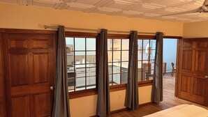 Una habitación con un ventanal grande, puertas de madera, un ventilador de techo y una cama.