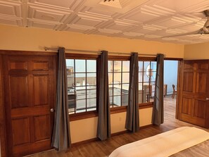 A room with a large window, wooden doors, a ceiling fan, and a bed.