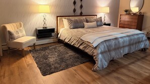 Un dormitorio con una cama, dos mesitas de noche con lámparas, una silla, un tocador y un espejo en la pared.