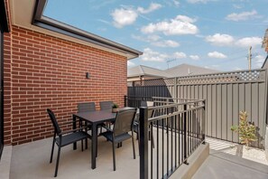 Un patio con una mesa, sillas, un muro de ladrillo y una valla de metal.