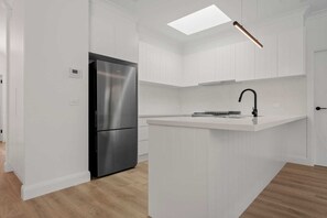 Una cocina moderna con armarios blancos, un refrigerador de acero inoxidable, un grifo negro y un tragaluz.