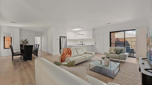A spacious living area with a dining table, two sofas, a coffee table, and a kitchen in the background.