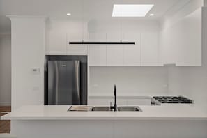 Una cocina moderna con armarios blancos, un refrigerador de acero inoxidable, un grifo negro y una estufa a gas.