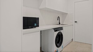 Un área de lavandería con lavadora, lavamanos y microondas.