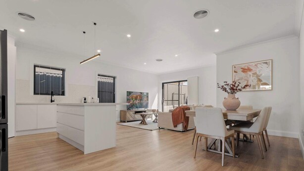 Una cocina moderna con armarios blancos, un comedor con mesa y sillas de madera, y una sala de estar con sofá y una mesa de centro.