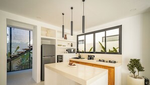 A modern kitchen with a large island, built-in appliances, pendant lighting, and a view through the window. - Uluwatu Surf Sanctuary Villa (Uluwatu)