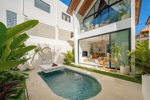 Una casa moderna con piscina, mobiliario exterior y un amplio ventanal que da a una sala de estar.