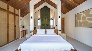 A large bed in a room with wooden beams, a stone wall, and a modern light fixture. - Uluwatu Surf Sanctuary Villa (Uluwatu)