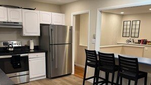 A modern kitchen with white cabinets, a stainless steel refrigerator, a gas stove, and a dining area with black chairs. - Fun 5 Bedroom Lakefront Cottage (Bethel)