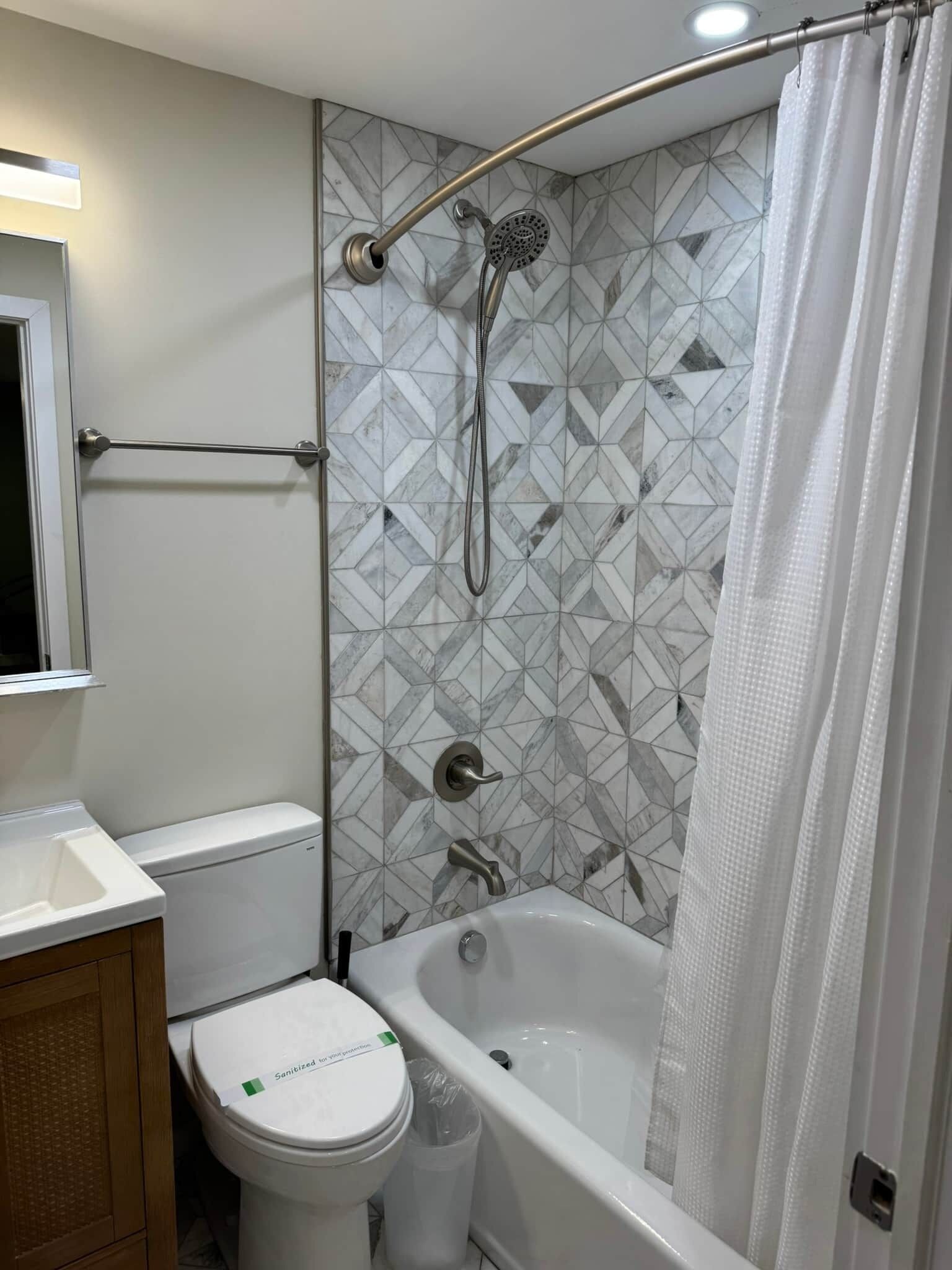 A bathroom with a shower, toilet, and sink, featuring geometric tile patterns.